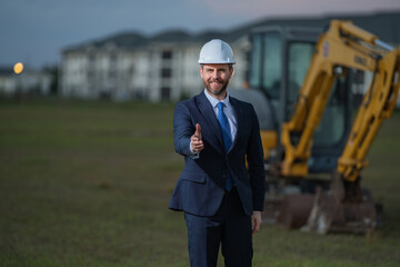 Construction business owner. Man in suit and hardhat halmet at building construction site. Civil engineer worker in front of house near excavator. Architect, supervisor investor, construction manager.