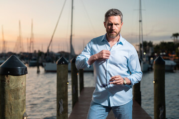 Millennial 40s man near the yacht. Portrait of fashion model outdoor. Fashion male posing near...