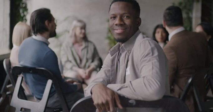 Portrait of cheerful African American man smiling sitting in circle of people enjoying group therapy smiling. Psychology and successful recovery concept.