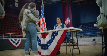 American citizens come to vote in polling station. Polling officer consults voters and gives them...