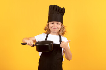 Funny kid chef cook with kitchen pot stockpot. Kid in cooker uniform and chef hat preparing food on...