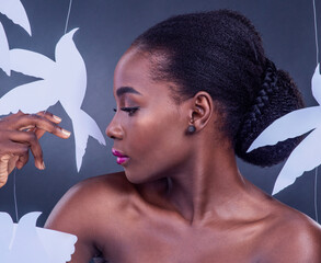 Black woman, paper bird and cosmetics for freedom, peace and wellness isolated in dark background. African model, beauty and abstract fantasy with makeup, skincare and creative animal art or origami