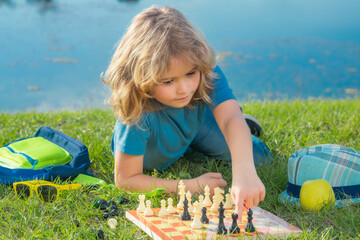 Chess game for kids. Child playing chess outdoor in park.
