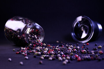 peppercorns scattered from a pepper shaker on the surface on a black background to add flavor and...