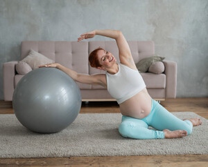 Pregnant woman doing side bends with a fitness ball at home.