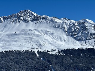 Obraz premium Beautiful sunlight and snow-capped alpine peaks above the Swiss tourist sports-recreational winter resorts of Valbella and Lenzerheide in the Swiss Alps - Canton of Grisons, Switzerland (Schweiz)