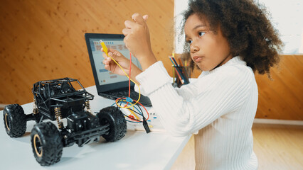 Smart african girl build robotic car while using wires while using laptop setting or writing prompt code. Skilled female student working on computer in STEM technology online classroom. Erudition.