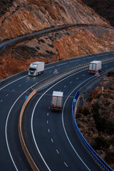 Three trucks with a refrigerated trailer driving along a curve on a highway, transporting food.