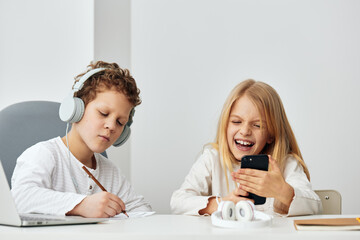 Boy and girl happily learning and playing together at home using laptops and tablets They are sitting at a table in the living room, wearing headphones and typing on their devices The room is filled