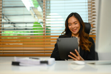 Successful businesswoman sitting at her workplace and using digital tablet - 797549707