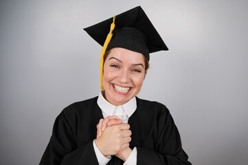 Caucasian woman in graduate gown dreamily holds her hands on her chest. 