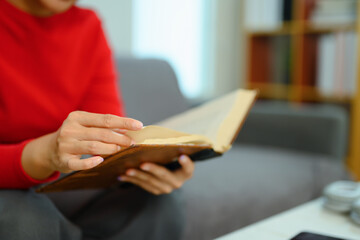 Closeup young woman in warm sweater reading book on couch at home