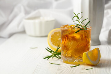 Cocktail with ice, rosemary and lemon slices on the white table.