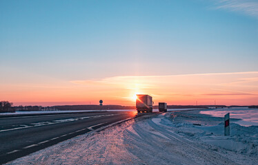 Semi truck driving along a snowy highway at sunset in winter
