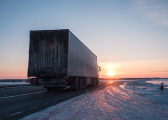 Semi truck driving along a snowy highway at sunset in winter