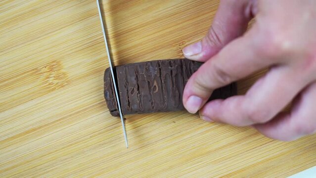 Cutting off thin slices of candy bar with a knife on the cutting board