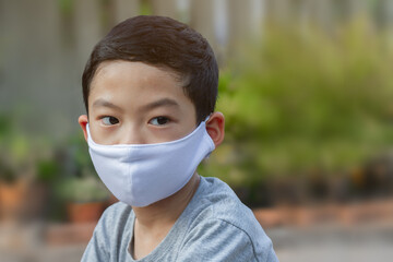 Asian black hair little boy aged 6-7 years old on outdoors area wearing white protective facemask...