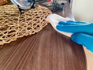 Person in electric blue gloves cleaning hardwood table with cloth