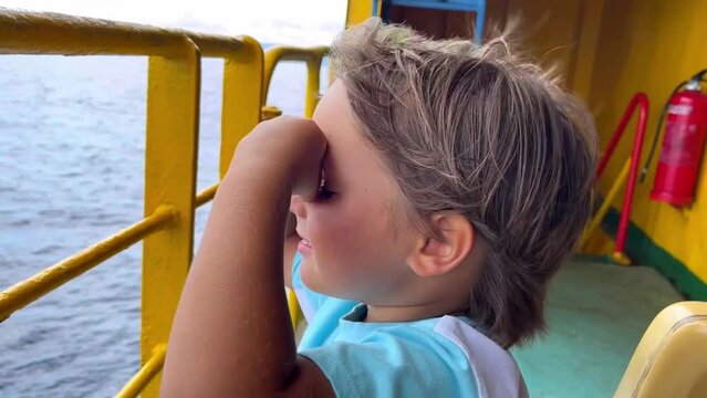 A little boy fists into binoculars and looks out at the sea. Slow motion picture of a child standing on a ship. High quality FullHD footage