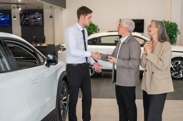 A salesman hands over the keys to a new car to an elderly Caucasian couple.