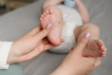 Mother gives baby foot massage to infant, close-up. Woman massages bare foot of a cute newborn in...