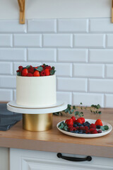white cake with red raspberries and strawberries in the kitchen, next to a plate of berries