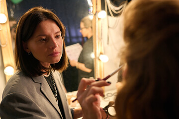 Portrait of make up artist putting blush on actress backstage by vanity mirror copy space