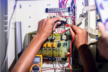 An electronics technician is using a digital meter to check a fire alarm control panel.