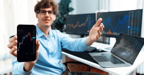 Successful young business trader showing dynamic stock market graph on smartphone, presenting...