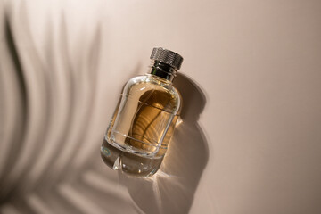 Golden perfume with leaf shadow on beige background, elegant bottle with transparent packaging,...