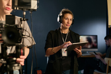 Waist up portrait of adult woman as production assistant working on set and wearing headset copy...