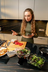 a young girl in love in a green dress in the kitchen preparing dinner according to a recipe from her phone
