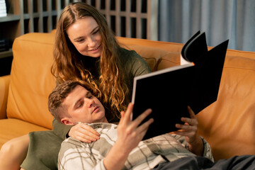 close up young couple in love on yellow sofa hugging and flirting guy reading a book