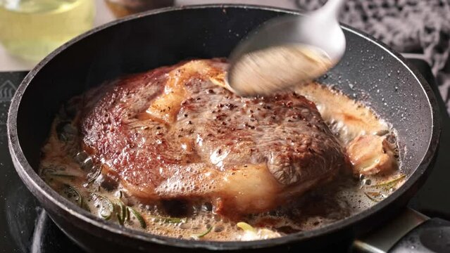 Chef pours melted butter on a juicy beef steak frying on a pan in the kitchen, close-up. Process of cooking delicious beef steak.