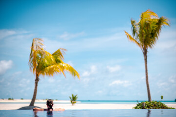 Woman gazing onto the beach from an infinity pool