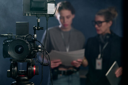 Front view closeup of professional digital video camera on stand in video production with blurred crew in background copy space