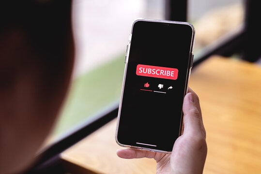 Close-up view of a woman using a smartphone to press red subscribe button on online media. Concepts of technology and following news, hot trends and new content on social media - Powered by Adobe