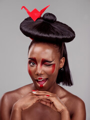 Creative beauty, wink and black woman with origami in studio isolated on dark background. Funny...