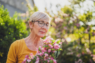 Happy senior woman enjoys in the smell of flowers in her garden.