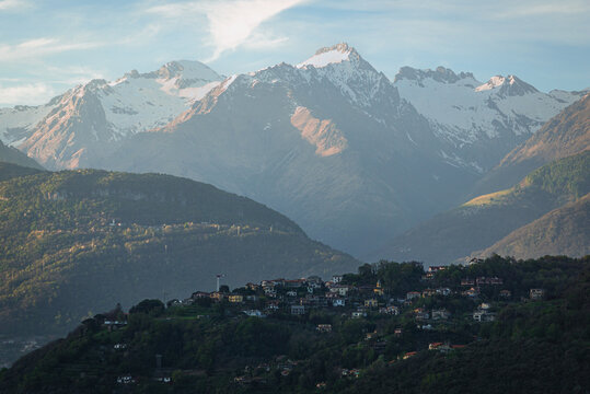 Scenic spring sunset over the Olgiasca peninsula on Lake Como, Italy. Breathtaking view of calm waters and snow-capped Alpine peaks contrasting with the warm evening light in Lombardy. - April 2024
