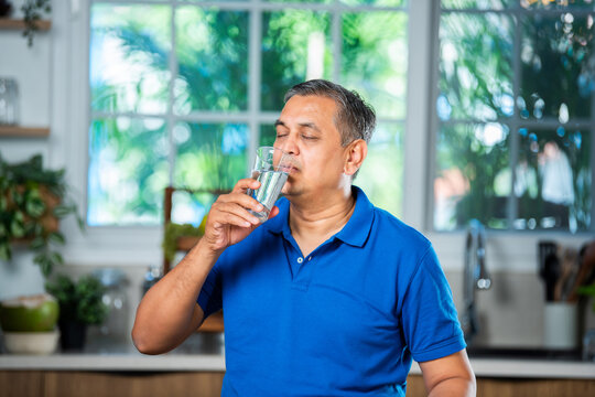 Indian asian mid age handsome man drinking plain water in a glass at home