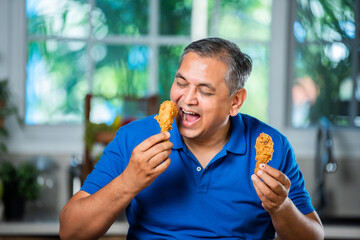 Indian asian mid age handsome man eating chicken leg piece with happiness