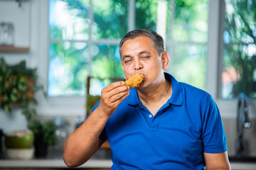 Indian asian mid age handsome man eating chicken leg piece with happiness