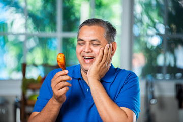 Indian asian mid age handsome man eating chicken leg piece with happiness
