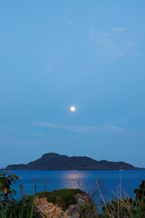 Fototapeta na wymiar 早暁の阿嘉島、天城（アマグスク）展望台。 西方の久場島にはまだピンクムーンの満月が空に残っている。 海には美しいムーンロードが見える。 日本国沖縄県島尻郡慶良間諸島の阿嘉島にて。 2021年4月27日撮影。 Amagusuku Observatory, Aka Island in the early morning. The full pink moon is still in the sky o