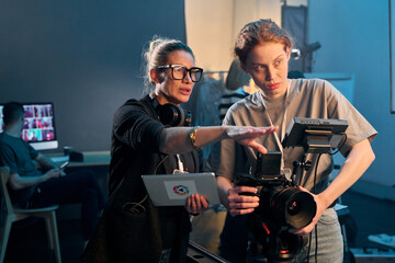 Waist up portrait of female director giving instructions working in video production and operating...