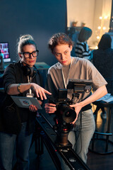 Vertical portrait of camerawoman operating professional video camera on rig with female director giving instruction