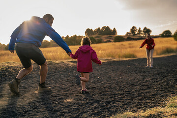 Adult and child holding hands while running toward a woman - Family outdoor adventure - joyful...