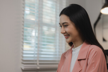 Fototapeta premium A beautiful young Asian woman is happily sitting in a private office. The atmosphere in a private office with female employees sitting in the room with smiles on their faces.