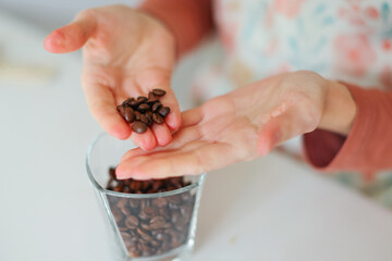 Close-up of girl's hands showing roasted coffee bean with blurred background behind. Shallow depth of field focused on coffee bean. Concept of individual approach to quality control.
